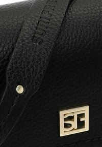 Borsa a mano in pelle nera con superficie testurizzata, ferrature di marca in tonalità oro e dettagli decorativi dorati sulla parte anteriore.
