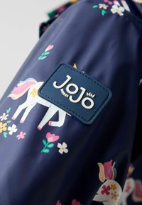 Ciemnoniebieska tkanina z kolorowymi wzorami jednorożców i kwiatów, z haftowaną prostokątną metką z brandingiem "JoJo maman bébé".
