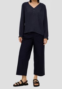 Mörkblå långärmad topp med V-ringning och placket med tre knappar, i kombination med vida mörkblå byxor och svarta sandaletter med remmar.