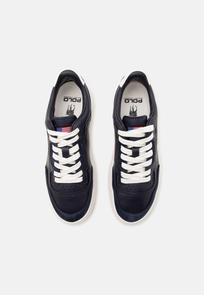 Ζευγάρι μαύρα sneakers Polo Ralph Lauren με λευκά κορδόνια και σόλες, με μικρή αμερικανική σημαία στη γλώσσα.