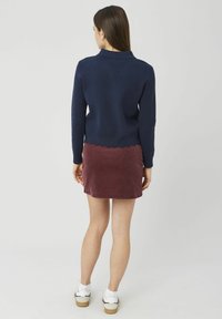 Pull en maille bleu marine avec un ourlet festonné, associé à une jupe en velours côtelé bordeaux, porté avec des chaussettes blanches et des chaussures plates crème.