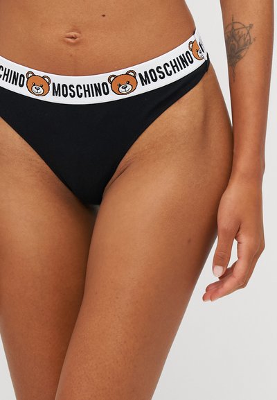 Black cotton thong with a white elastic waistband featuring a teddy bear and "MOSCHINO" text. Smooth texture, minimal coverage design.