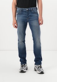 Blauwe denim jeans met een rechte snit, vijf zakken en subtiele vervaging. Gecombineerd met zwart-witte sneakers.