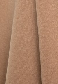 Tessuto beige con una trama liscia e morbida. Il materiale sembra leggero e elastico, con un sottile motivo di tessitura uniforme.