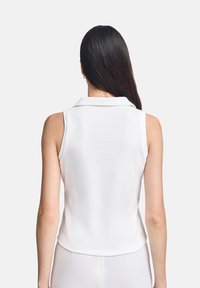 Top bianco senza maniche con colletto, caratterizzato da una texture a coste, con orlo arrotondato e dettagli di cucitura sottili sul retro.