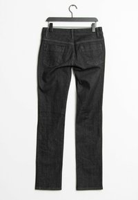 Los jeans de mezclilla negra cuelgan de una percha negra, presentan un ajuste slim, dos bolsillos traseros y detalles de costura sutil a lo largo de las costuras.
