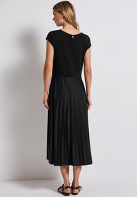Robe noire à manches courtes, haut ajusté et jupe plissée. Présente un col rond et un bouton décoratif à l'arrière.