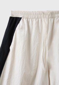 Gros plan sur un short blanc avec des panneaux latéraux noirs, doté d'une taille élastique et d'un cordon à l'avant.