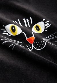 Tessuto nero con una stampa di faccia di gatto in stile cartone animato; presenta grandi occhi gialli, un naso rosso e baffi bianchi su una superficie morbida.