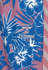 Blommig sportkläder med blå och vita hibiskusmönster på en rosa bakgrund, med en grå broderad logotyp och en texturerad detalj.