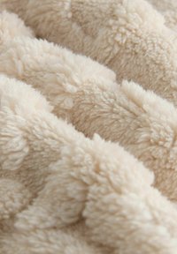 Tessuto peluche beige con una texture morbida e soffice, che presenta un motivo ondulato e altezze variabili su tutta la superficie.