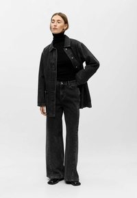 Black denim jacket with a collar, paired with a black turtleneck and wide-leg jeans. Smooth texture and button details are visible.