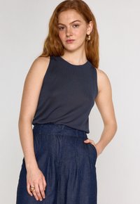 Top senza maniche di un blu scuro con scollo rotondo, realizzato in tessuto a coste; abbinato a pantaloni in denim a vita alta con tasche laterali.