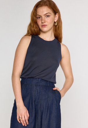 Top senza maniche di un blu scuro con scollo rotondo, realizzato in tessuto a coste; abbinato a pantaloni in denim a vita alta con tasche laterali.