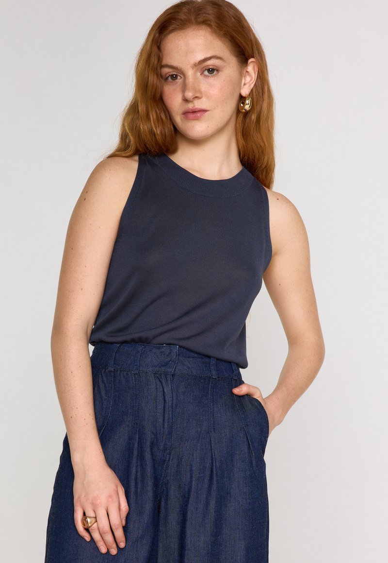 Top senza maniche di un blu scuro con scollo rotondo, realizzato in tessuto a coste; abbinato a pantaloni in denim a vita alta con tasche laterali.