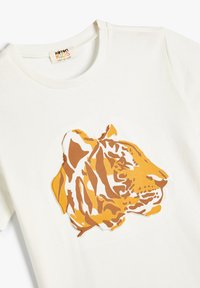 Hvid bomuld t-shirt med et stiliseret tigerhoved grafisk design i nuancer af orange og brun, med kontrastfulde hvide konturer.