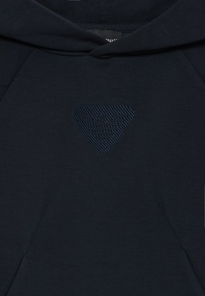 Námornícka mikina s textúrovaným trojuholníkovým logom v strede, obsahujúca vrecko a klasickú kapucňu so šnúrkou. Mäkká tkanina s textúrou.