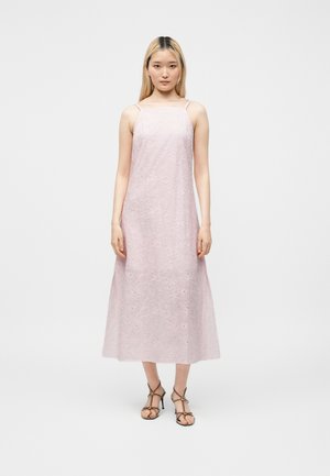 Egyenes szőke hajú fiatal nő világos rózsaszín, hímzett, ujjatlan midi ruhát és fekete, pántos, magas sarkú szandált visel.