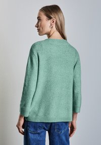 Mintgroene, zachte trui met een iets oversized pasvorm, driekwartmouwen en ribbelranden, gecombineerd met denim jeans.
