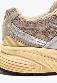 Chunk of beige and tan sneaker heel with textured sole, mesh fabric, suede accents, and "MYTHOS STAR" branding in silver strip on side.