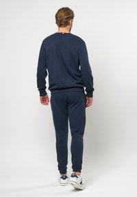 Marinblå sweatshirt och matchande joggers i ett mjukt material. Har ribbade muddarna och midjan med en diskret logotypdetalj på baksidan.