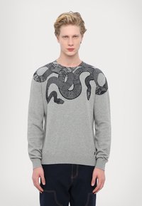 Maglione grigio con maniche lunghe, caratterizzato da un design di serpente nero sulle spalle. Il materiale appare texture con orlo e polsini a coste.