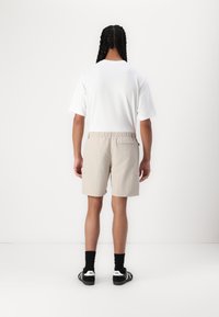 Lys beige shorts med elastisk midjebånd, sidelommer og en baklomme. Kombinert med en enkel hvit t-skjorte og svarte sokker.