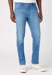 Jeans de denim azul claro con corte recto, que presentan detalles de costura sutil y diseño clásico de cinco bolsillos, combinados con zapatillas blancas.