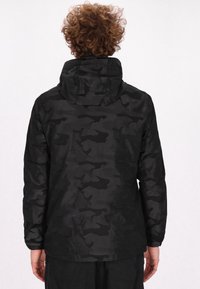 Sort camouflagejakke med hætte, der har en tekstureret overflade. Designet inkluderer en løs pasform og elastiske manchetter for komfort.