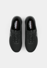 Black athletic shoes with a textured upper, elastic laces, and a wide fit design, featuring a memory foam insole and curved toe cap.