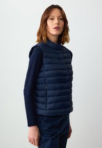 Marineblaues Steppweste aus quiltierter Baumwolle, mit hohem Kragen und ärmellosem Design. Reißverschlussdetails an der Seite.