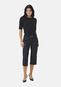 Sort tætsiddende top med korte ærmer, parret med mørk denim cropped bukser og sorte spidse hæle. Enkel bælte detalje om taljen.