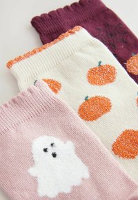 Drei Paar Socken: ein lila Paar mit Spinnenweben, ein cremefarbenes Paar mit orangefarbigen Kürbissen und ein pinkes Paar mit einem plüschigen weißen Geist.
