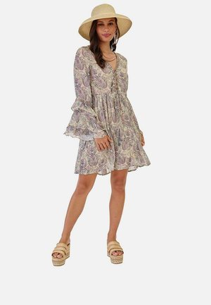 Mujer con vestido de manga larga con estampado de cachemira, sombrero de paja de ala ancha, pendientes de aro y sandalias de plataforma con tiras trenzadas.