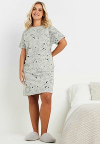 Cotonato grigio a maniche corte con motivi celestiali di soli, lune e stelle. Tessuto morbido, taglio a ginocchio, indossato con pantofole pelose.