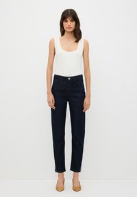 Jeans de mezclilla oscura con cintura alta, piernas ajustadas y cierre de botón. Combinado con una camiseta de tirantes blanca de canalé. Detalles en el dobladillo.