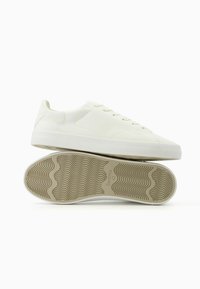 Vita sneakers med en slät läderöverdela, rund tåkonstruktion och platta snören. Gummisålen har ett vågigt mönster. Minimalistisk design utan synlig branding.