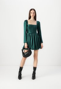 Grön satin klänning med pösiga långa ärmar, texturerad bodice och utsvängd kjol. Matchas med en svart läderhandväska och knähöga svarta stövlar.