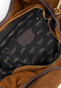 Interieur van een bruine suede handtas met zwarte stoffen voering, voorzien van een gouden "VENEZIA" patroon, een ritsvak en gouden rits hardware.