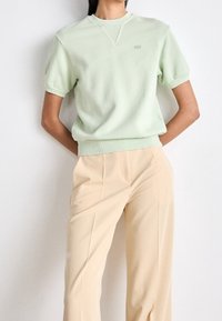 Light green short-sleeve sweatshirt with a crew neck and ribbed accents, paired with beige wide-leg trousers, smooth fabric texture.