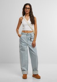 Jeans anchos de tiro alto en azul claro con puños enrollados, combinados con un top corto blanco. Botas de gamuza marrón y un bolso de hombro beige completan el look.