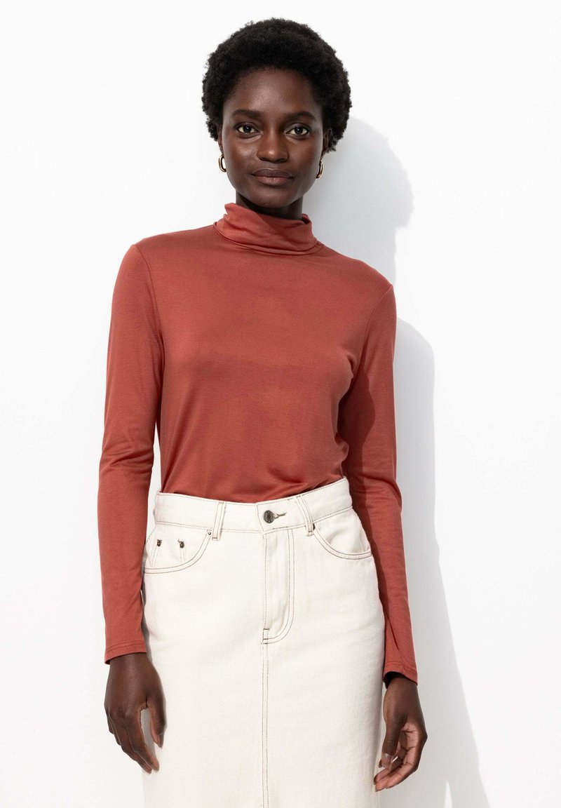 Un haut à col roulé long en rouille associé à une jupe en denim blanche. Le tissu a l'air lisse, avec une coupe ajustée et un design minimaliste.