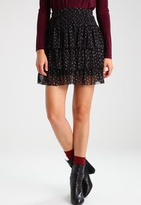 Falda mini negra de capas con una cinturilla fruncida, presenta un patrón sutil. Combinada con botas negras hasta el tobillo y calcetas burdeos.