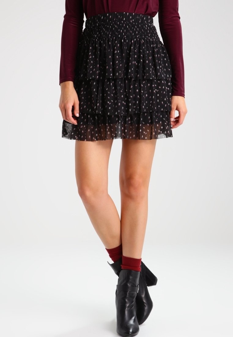 Falda mini negra de capas con una cinturilla fruncida, presenta un patrón sutil. Combinada con botas negras hasta el tobillo y calcetas burdeos.