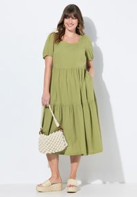 Grünes, Kleid mit puffärmeligen, gestaffelten Kleidern und quadratischem Ausschnitt aus strukturiertem Stoff. Kombiniert mit einer cremefarbenen gewebten Tasche und Plateausandalen.