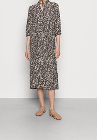 Abito midi navy con leggero motivo astratto, scollo a V con dettaglio a fiocco, maniche a tre quarti, tessuto fluido, sandali piatti beige.