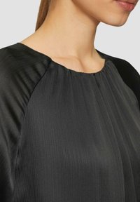 Zwarte, geplooide blouse met een ronde halslijn; gestructureerde stof creëert verticale strepen; gladde mouwen; lichte glansafwerking.