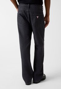 Wijde donkergrijze spijkerbroek van denim, met twee achterzakken en een klein driehoekig logoplaatje op de rechterzak.