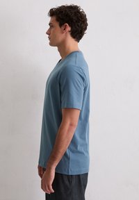 Jasnoniebieska bawełniana koszulka z dekoltem w kształcie litery V, krótkimi rękawami i luźnym krojem, prezentowana na męskim modelu z boku.