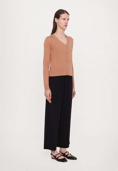 Cardigan din lână bej cu decolteu în V și cinci nasturi, asociat cu pantaloni negri largi și pantofi slip-on maro.